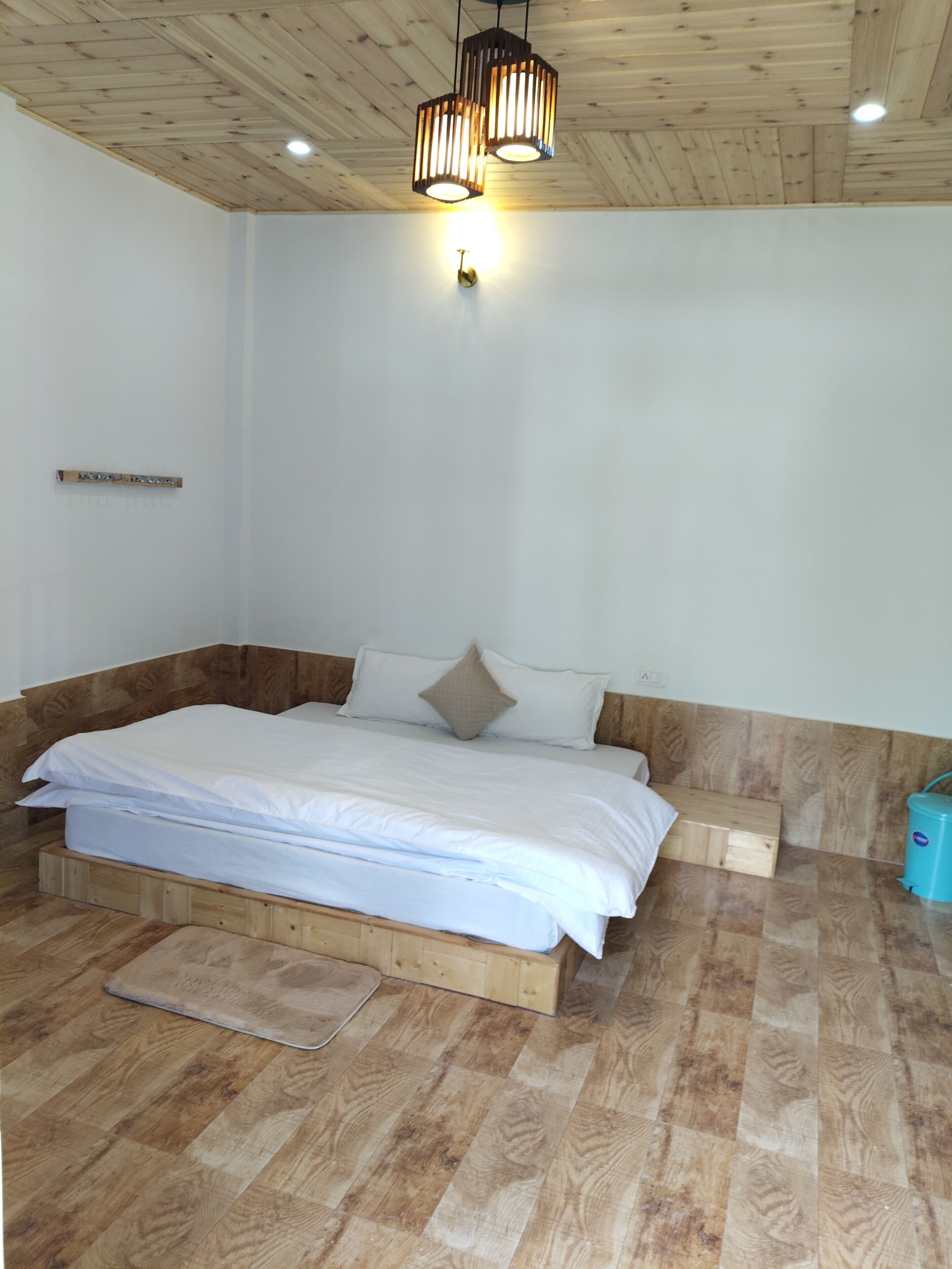 A bedroom with a wooden headboard, a bed with white bedding, a wooden floor, and a ceiling light fixture.