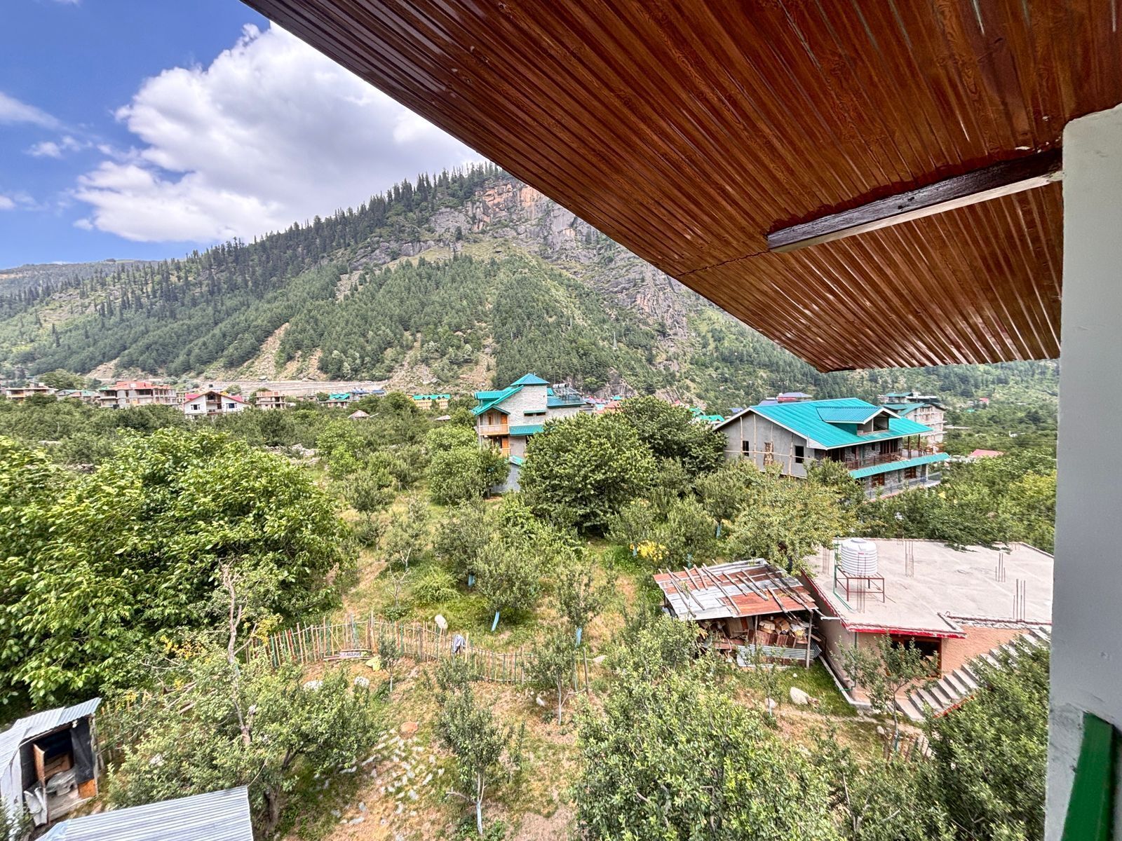 A mountainous landscape with several buildings, including a prominent house with a green roof and a smaller structure with a red roof.