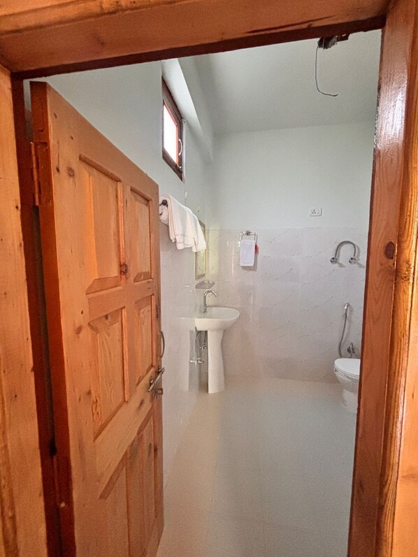 A bathroom with a wooden door, a sink, a toilet, and a shower.
