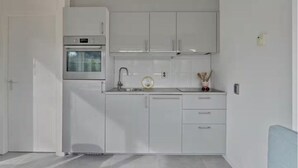 A compact kitchen with white cabinets, a built-in oven, and a sink. - Villa Dune I (Ouddorp)