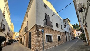 A narrow street with buildings on either side, a stone building with a white facade, and a blue parking sign. - HOLIDAY COTTAGE VILLALONGA RURAL (Vilallonga)