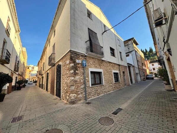 A narrow street with buildings on either side, a stone building with a white facade, and a blue parking sign. - VILLALONGA RURAL VACATION HOME (Vilallonga)