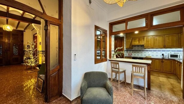 A spacious living area with a wooden-framed doorway leading to a kitchen. A comfortable armchair is positioned near a small table with two chairs. - HOLIDAY COTTAGE VILLALONGA RURAL (Vilallonga)
