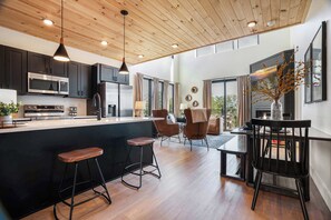 A modern kitchen with dark cabinets, stainless steel appliances, and a wooden ceiling.