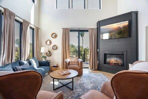 A modern living room with a fireplace, a sofa, a coffee table, and a television mounted on the wall. - Private Indoor Pool, Spacious Deck, Mountain Views (Sevierville)