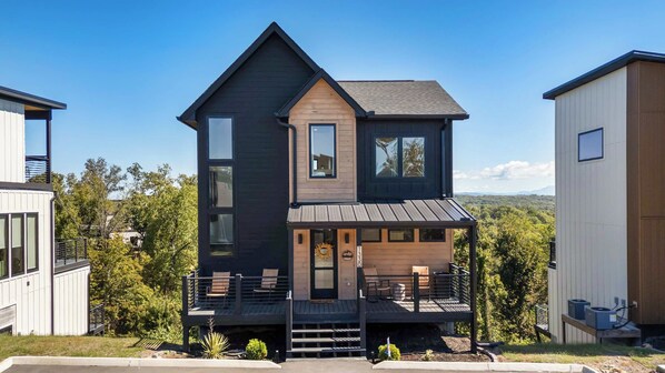 A two-story modern house with a balcony, a front porch, and a view of the surrounding landscape.