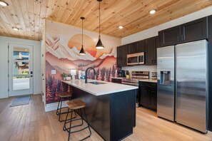 A modern kitchen with a wooden ceiling, stainless steel appliances, and a mountain-themed wall mural. - Private Indoor Pool, Spacious Deck, Mountain Views (Sevierville)
