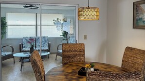 A dining area with wicker chairs, a round table, and a hanging light fixture.