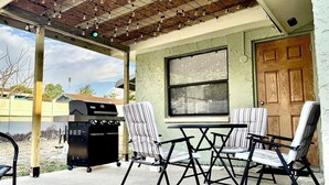 An outdoor patio with a grill, folding chairs, and a pergola with string lights.
