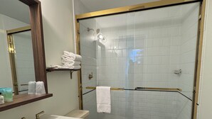 Een badkamer met een wit wastafelmeubel, gouden kranen, een toilet en een douche met glazen wanden, en een zwart-wit betegelde vloer.
