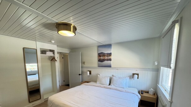 Hotelkamer met groot bed, nachtkastje, spiegel, kledingkast en raam met uitzicht op een meer.