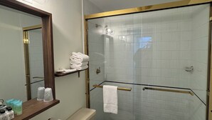Een badkamer met een witte wastafel, toilet, een douche met glazen wanden en een spiegel met gouden lijst.