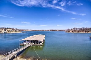 A riverfront dock with a covered seating area, a pedestrian bridge, and a clear view of the river and distant buildings.