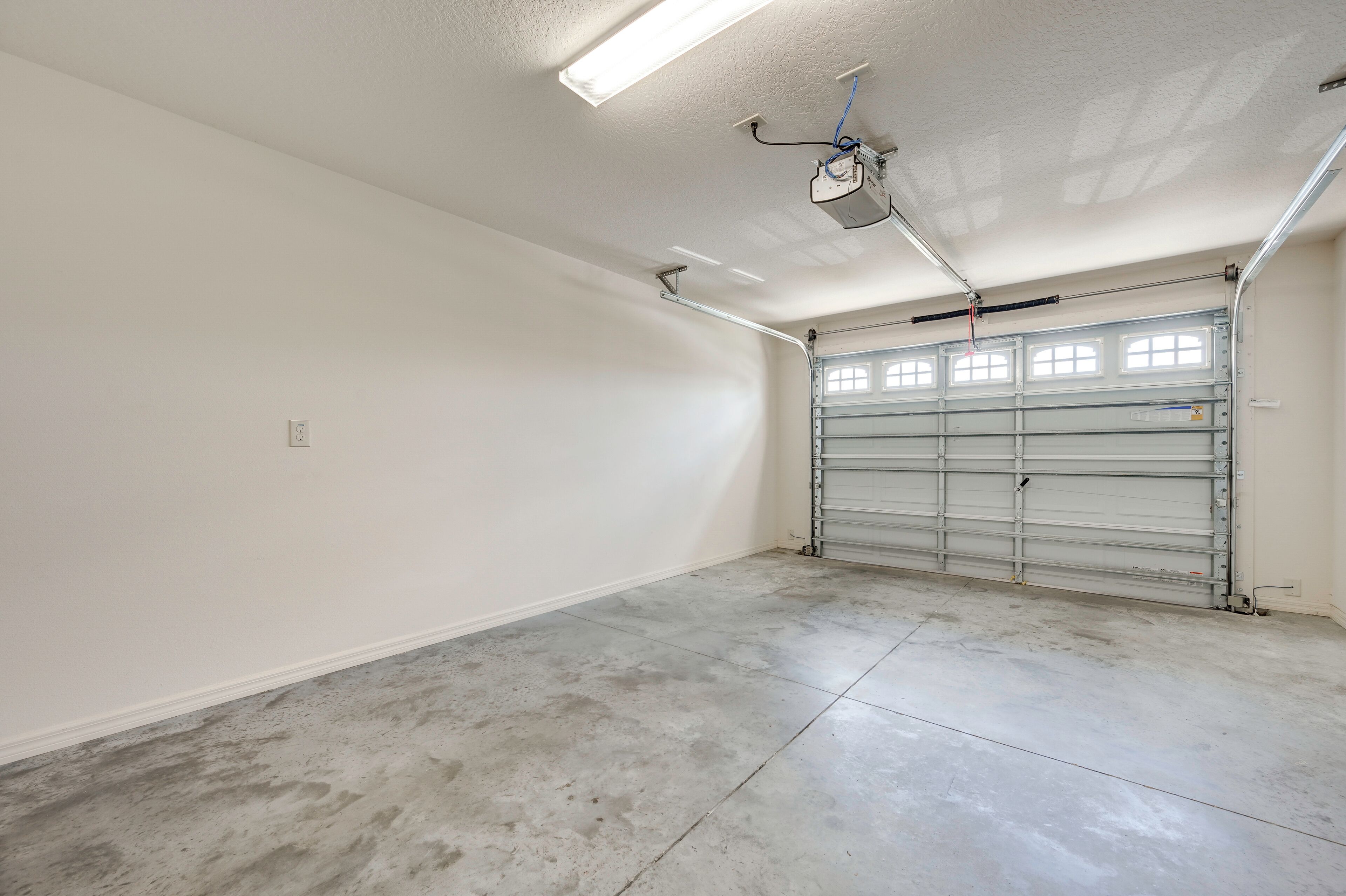 Eine saubere, leere Garage mit einer Metalldoortür, Deckenleuchten und einem Deckenventilator.
