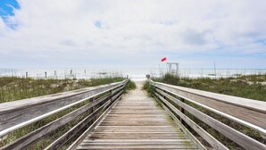 A wooden boardwalk leading to a beach with a red flag indicating caution. - Walk to the Waves: Coastal Kure Beach Retreat (Kure Beach)
