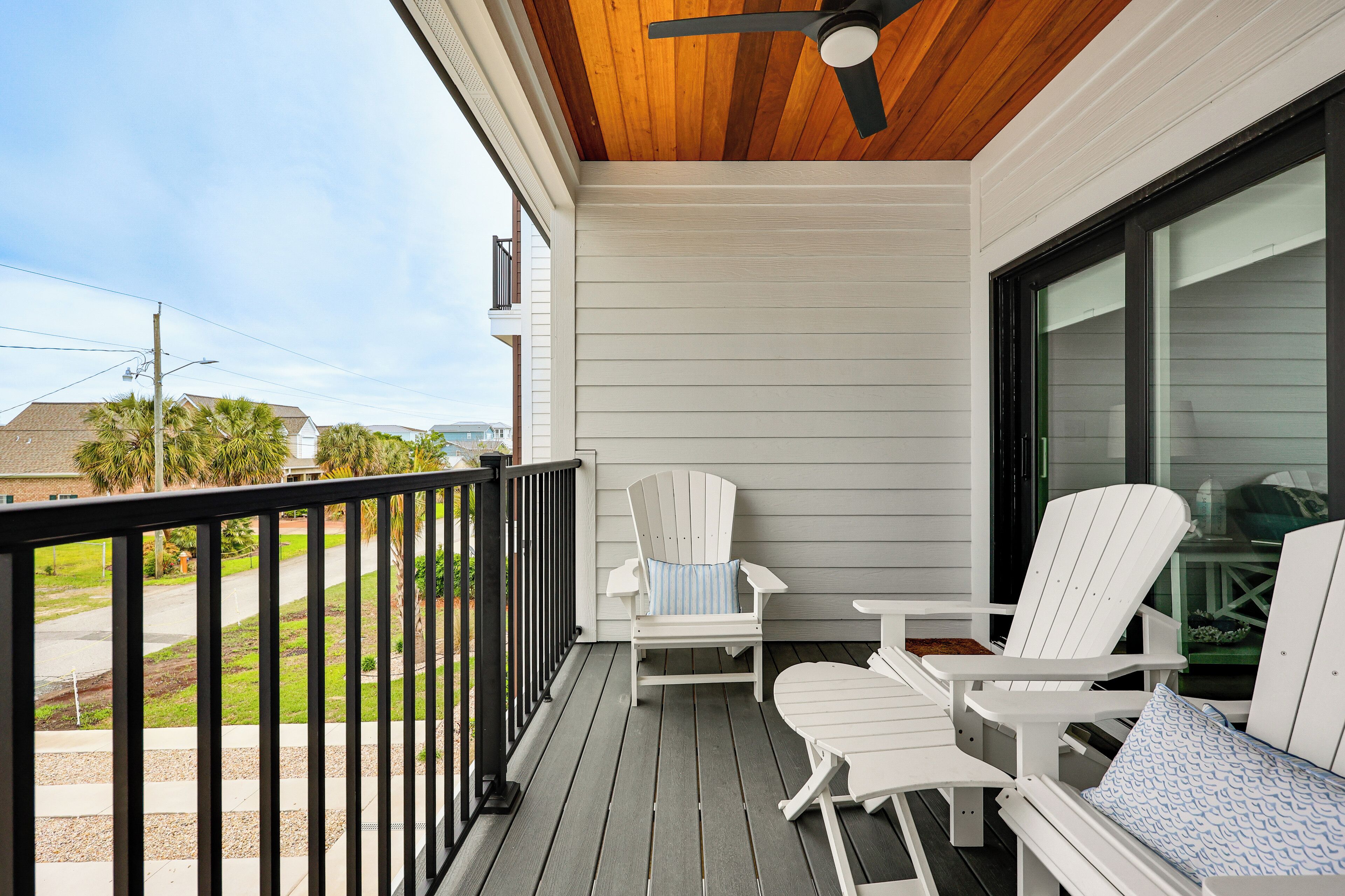 Une véranda couverte avec des fauteuils Adirondack blancs, une table et un ventilateur de plafond.