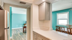 Een keuken met turquoise wanden, een wit aanrecht en houten stoelen.