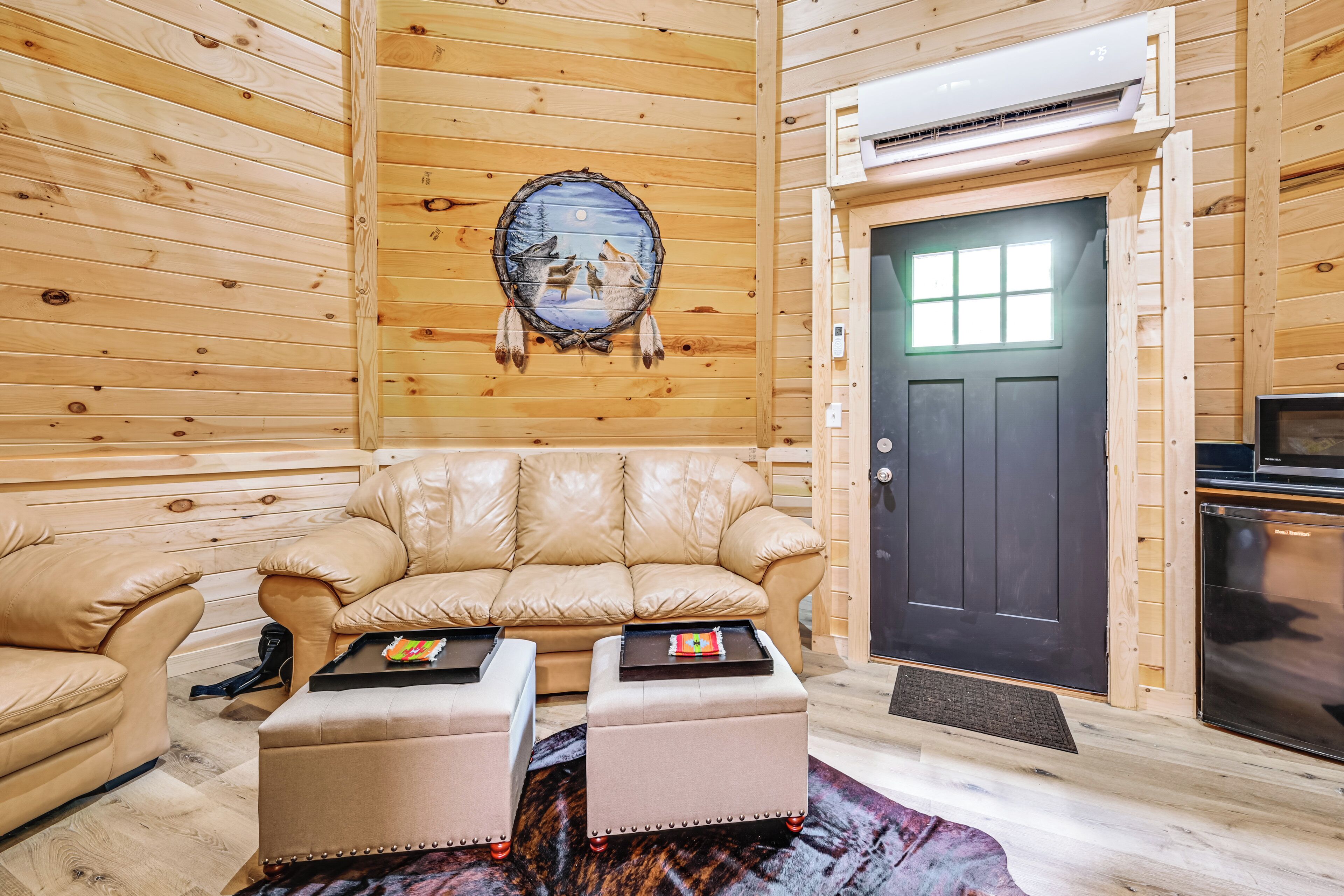 A cozy log cabin interior with a leather sofa, ottoman, and a dreamcatcher on the wall.