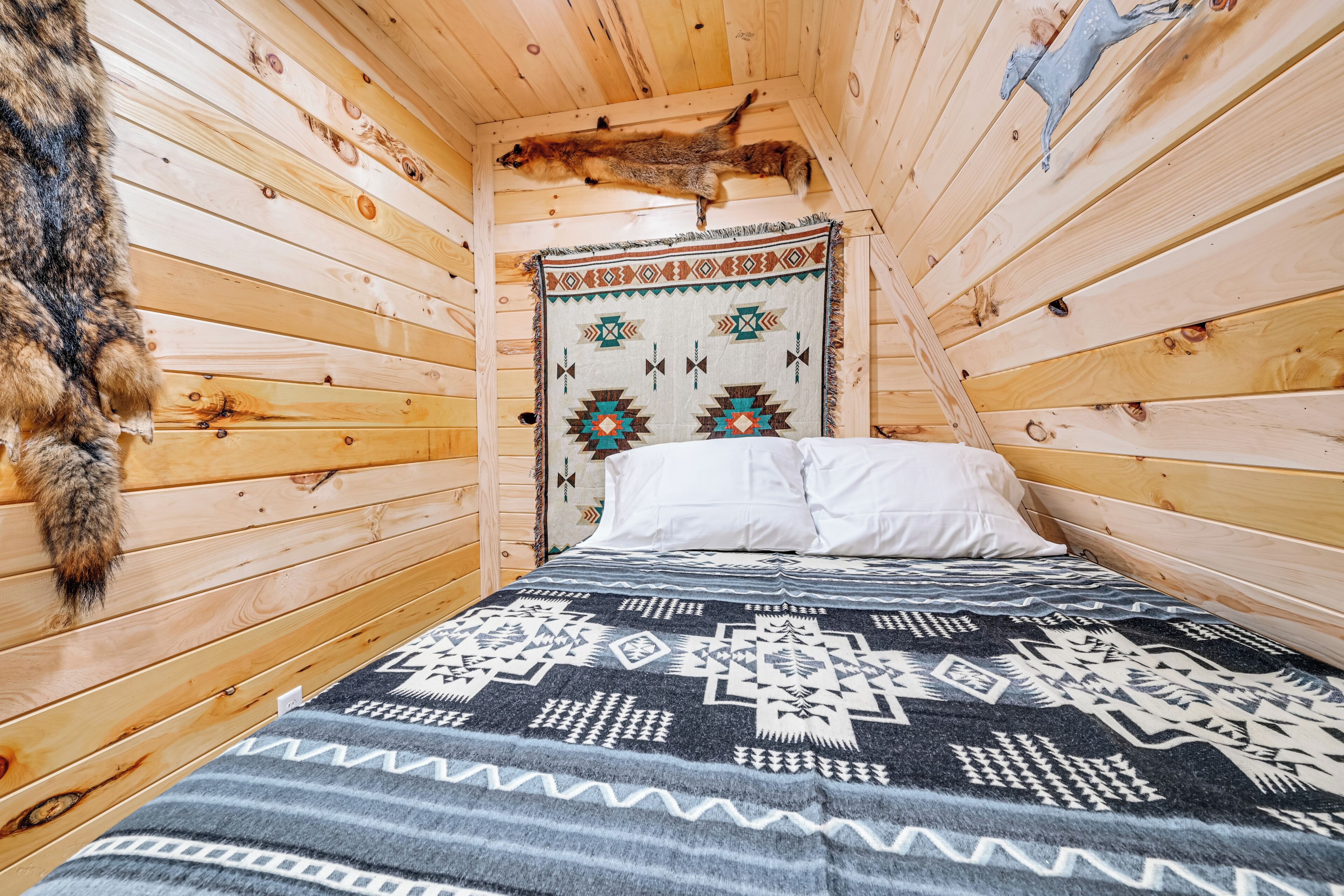 A wooden cabin room with a bed, a patterned blanket, and a fur rug.