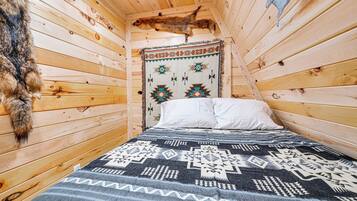 A wooden cabin room with a bed, a patterned blanket, and a fur rug.