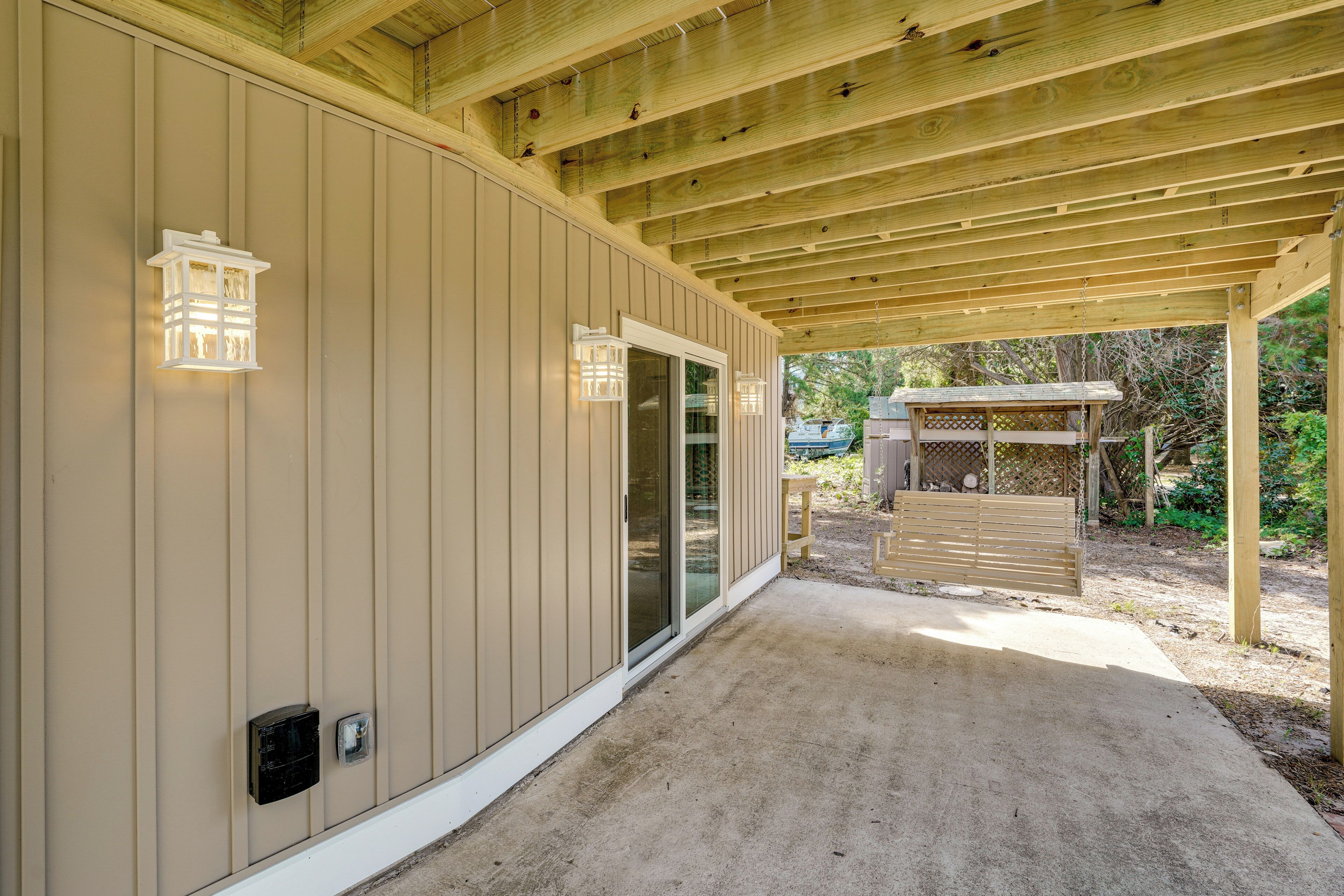 A covered patio area with a wooden ceiling and beige siding walls.