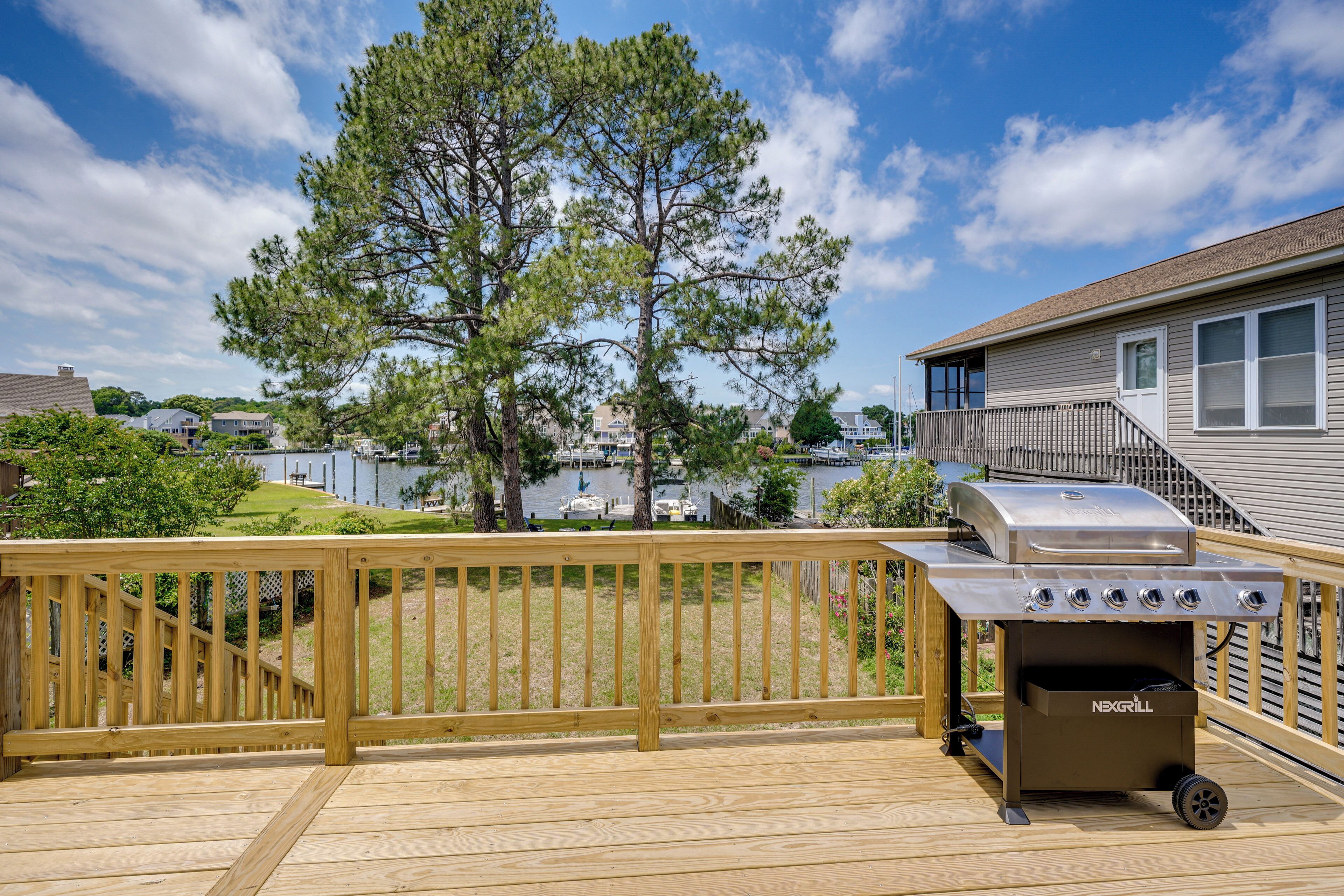 A wooden deck with a grill and a view of houses and a tree.