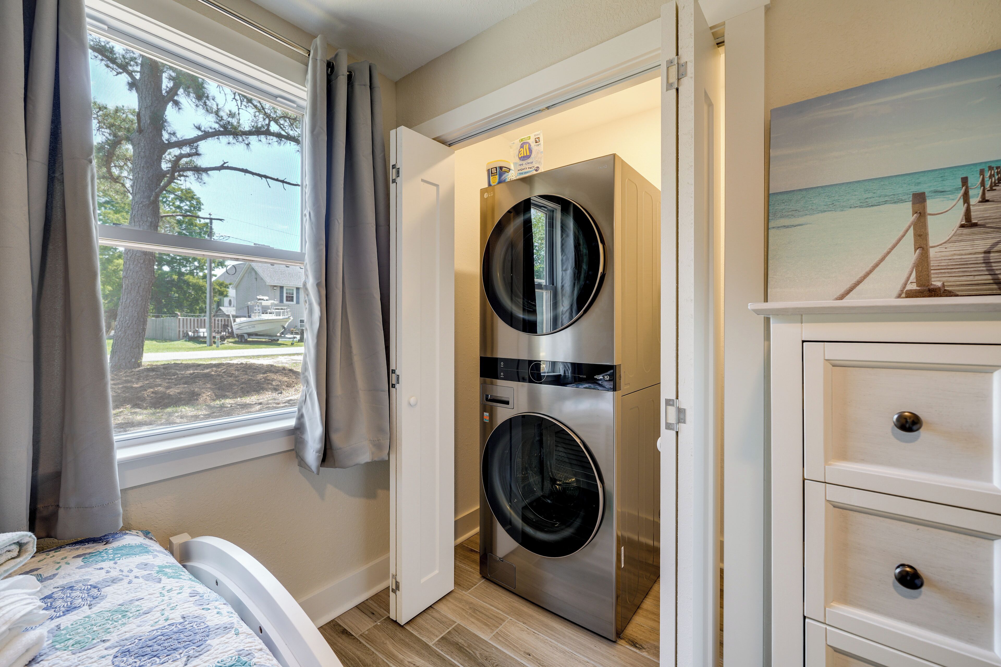 Une buanderie équipée d’un lave-linge et d’un sèche-linge à chargement frontal, un lit recouvert d’une couvre-lit à motifs et un tableau représentant une jetée accroché au mur.