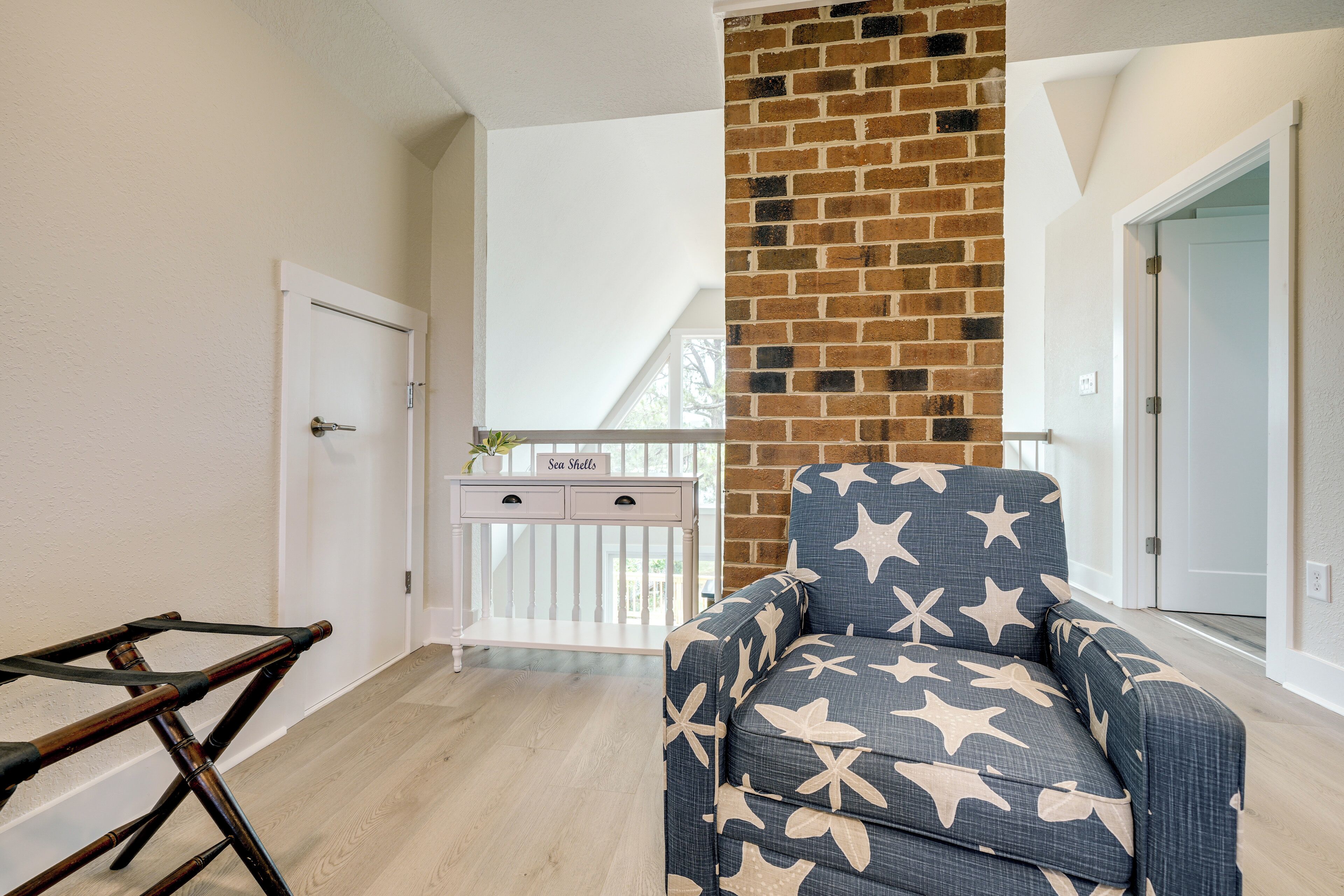 Un salon avec un fauteuil bleu orné d’un motif en étoile, un mur d’accent en briques et une porte blanche.