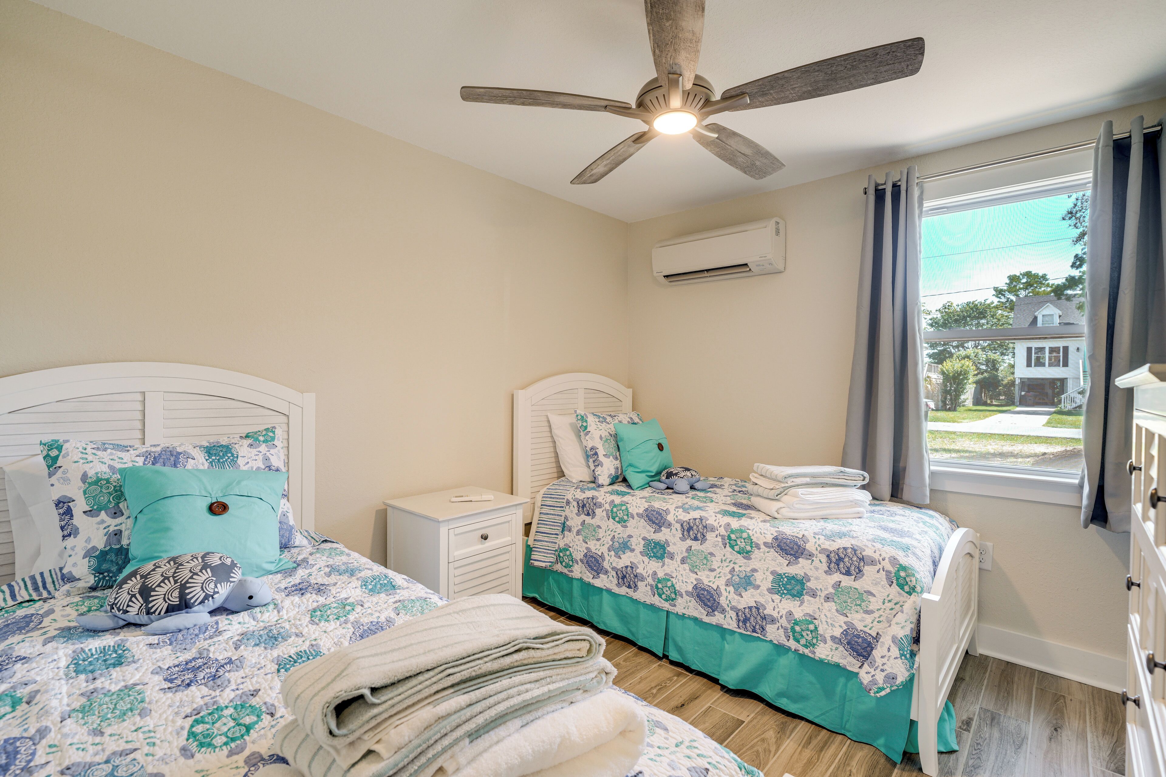 A bedroom with two beds, a ceiling fan, an air conditioning unit, and a window with curtains.