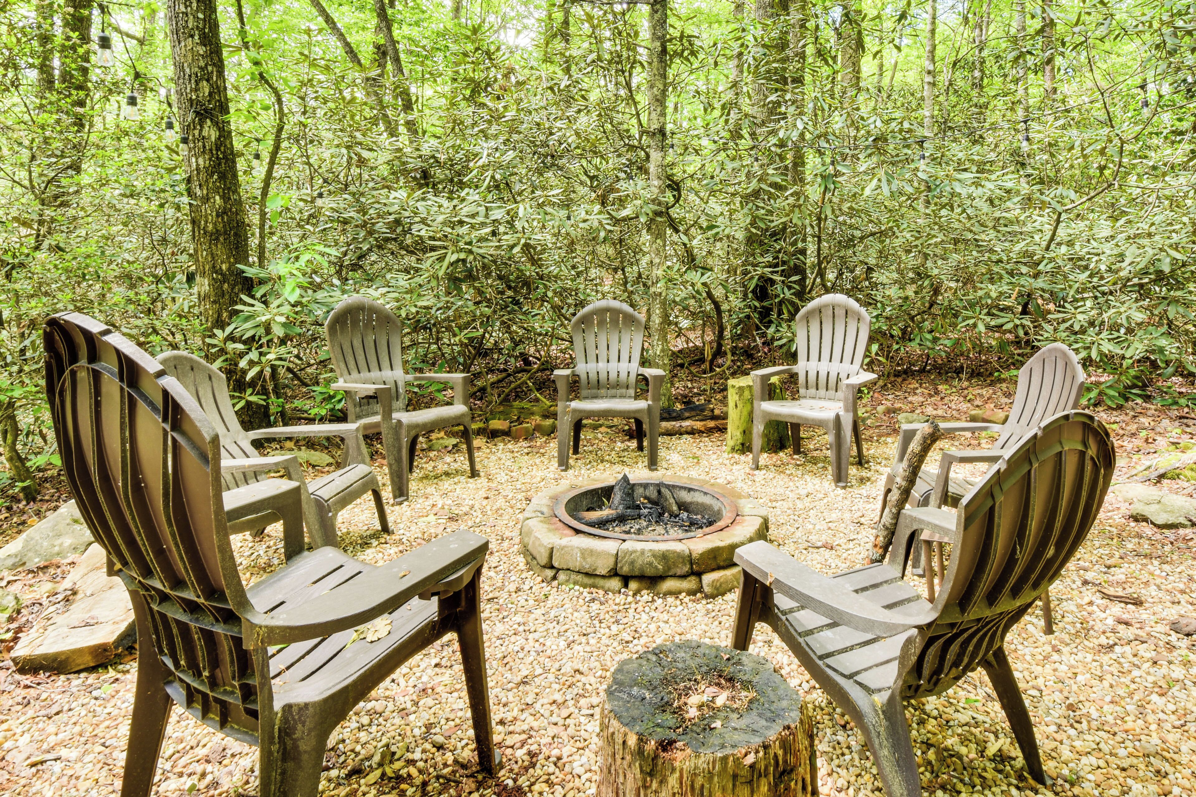A circular seating arrangement around a central fire pit in a forested area with trees and rocks.