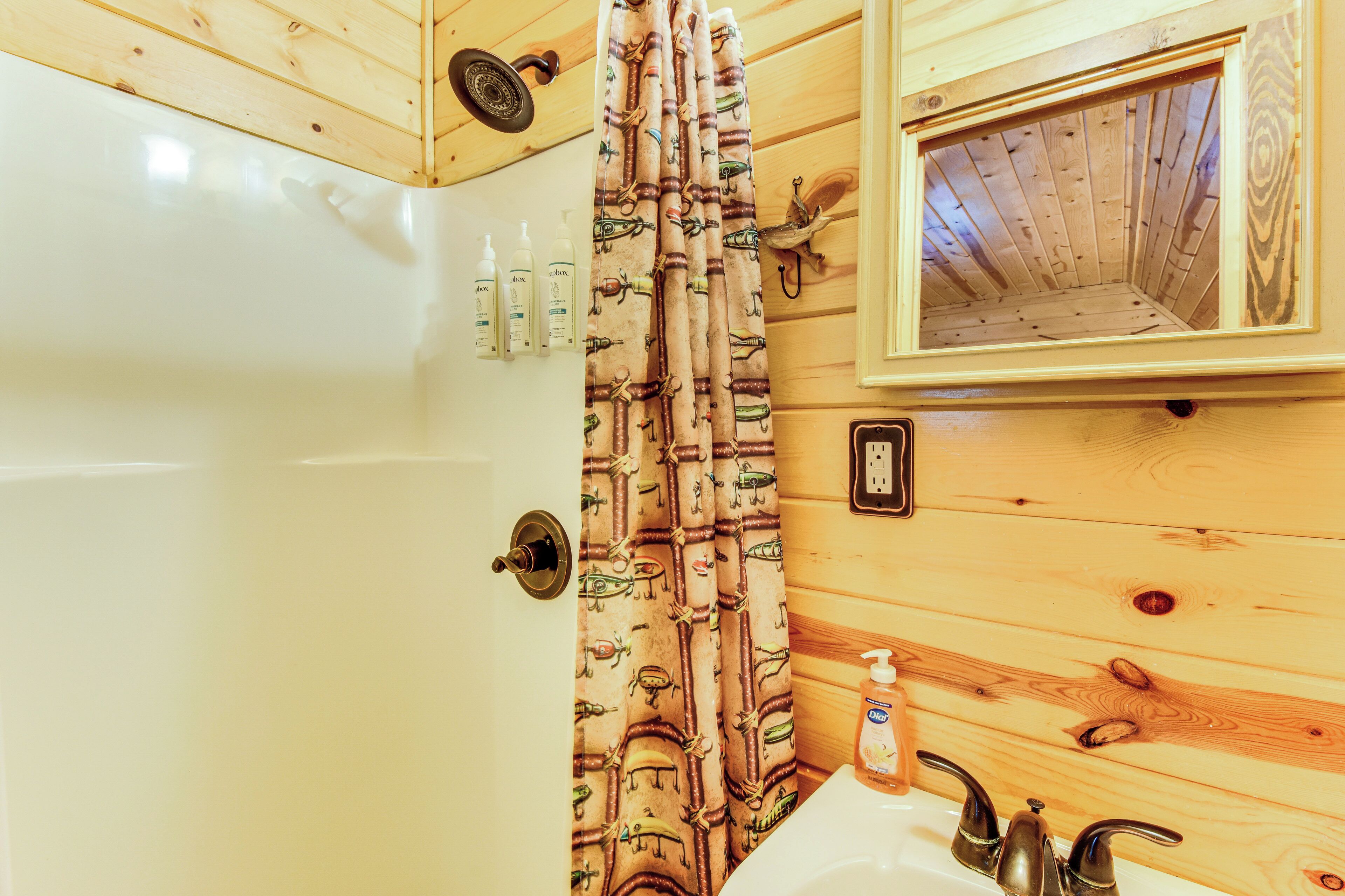 A bathroom with a bathtub, a shower curtain with a nautical theme, a mirror, and a sink with a soap dispenser.