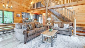 A spacious log cabin interior with a large living area, a kitchen, and a staircase leading to an upper level.