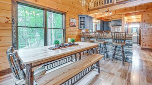 A wooden cabin interior with a dining area, kitchen, and a loft bedroom.