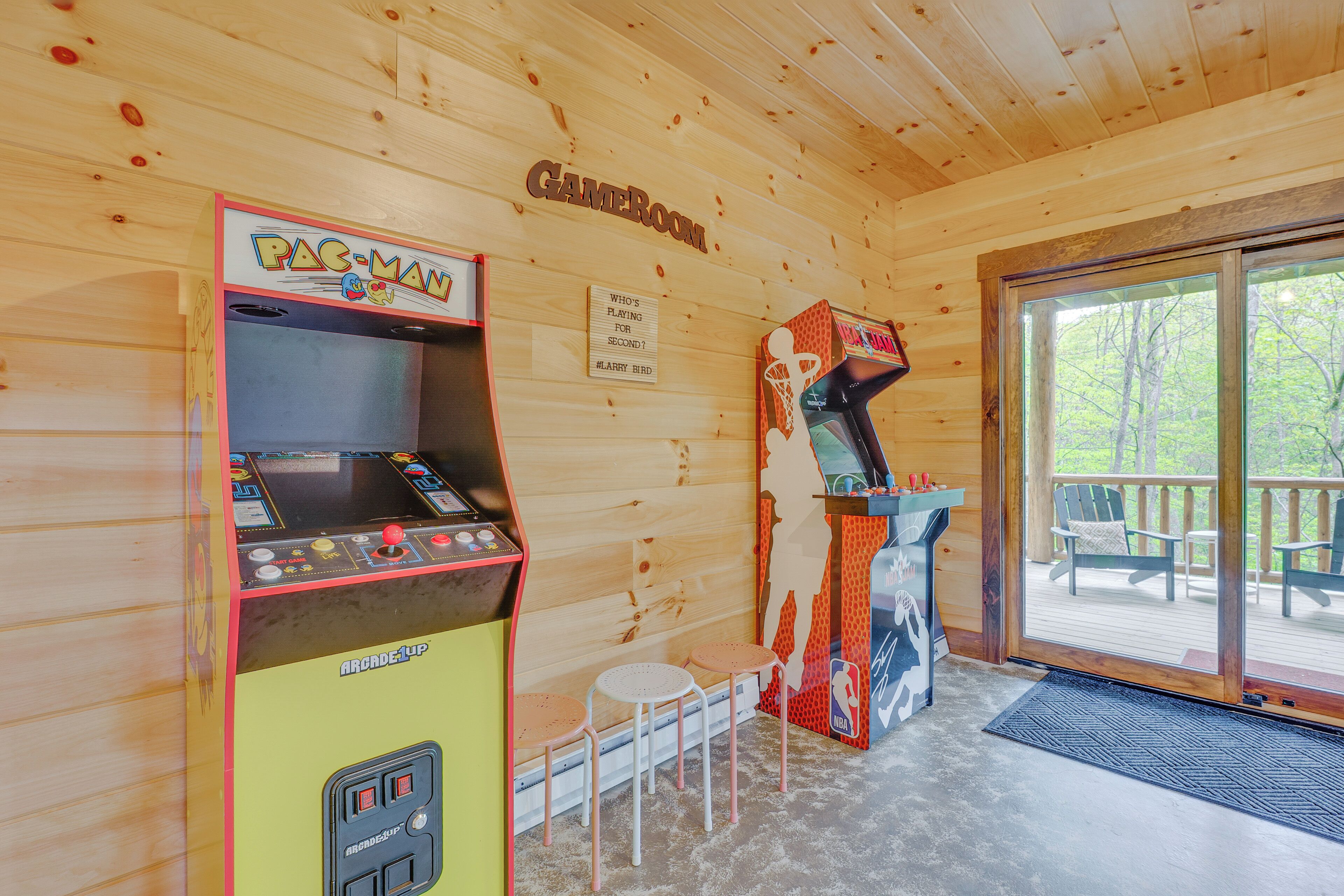 A wooden interior with Pac-Man and Donkey Kong arcade games, a sign reading "Who's playing for second?", and a deck with outdoor seating.