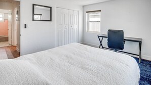 A bedroom with a bed, a desk, a chair, a window, and a door.