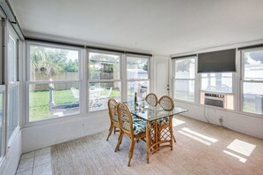 A sunlit room with a glass table and wicker chairs, large windows, and a view of a backyard. - Walk to Ocean: Cozy Home w/ Yard in Ormond Beach! (Ormond Beach)