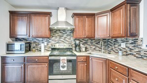 A kitchen with wooden cabinets, a stainless steel stove, a microwave, and a tiled backsplash.