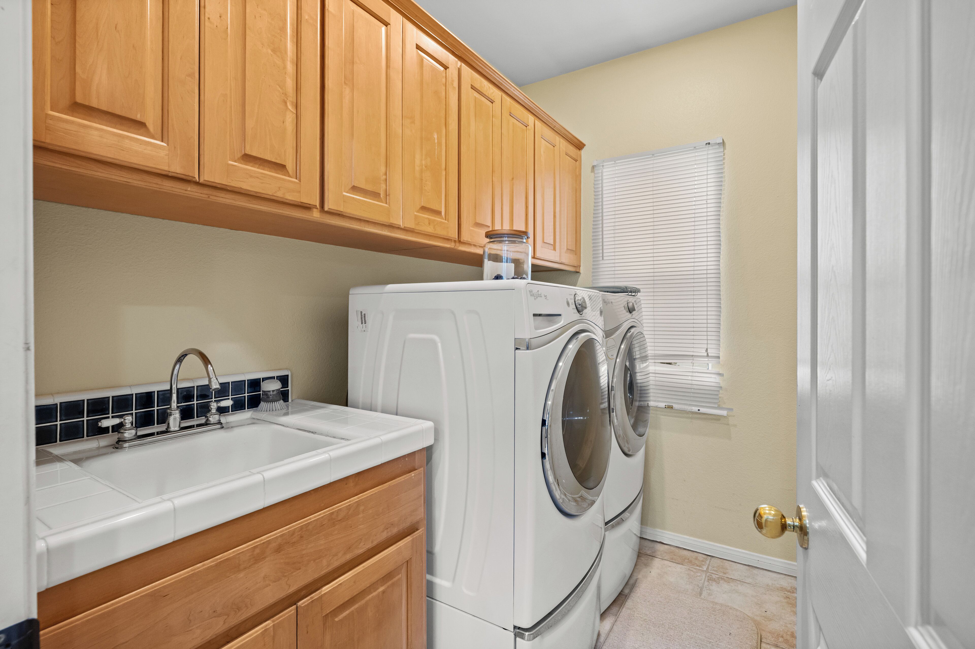 A laundry area with a washing machine, a sink, wooden cabinets, and a door.