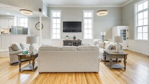 A spacious living room with a large sofa, a coffee table, and a television. There is a kitchen area with cabinets and a refrigerator. - Unique Church Turned Family Retreat: Relax & Enjoy (Alliance)