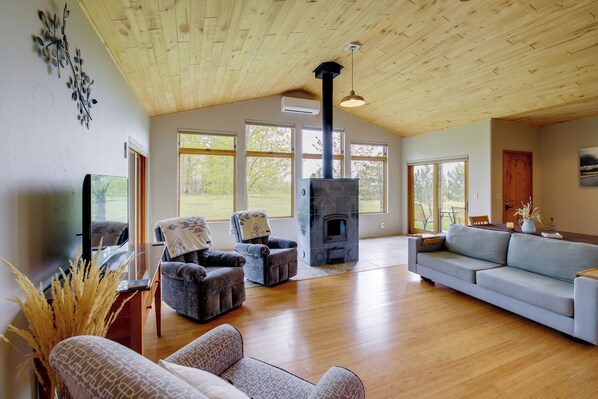 A spacious living room with a wooden ceiling, a fireplace, a sofa, and two armchairs.