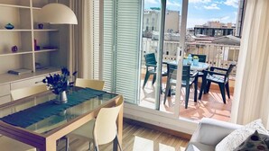 A modern living room with a glass dining table, a sofa, and a balcony with outdoor furniture.