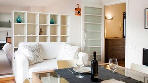 A modern living room with a white sofa, a glass dining table set for two, and a bookshelf with decorative items. - ATTIC BARCELONA CENTER (Barcelona)