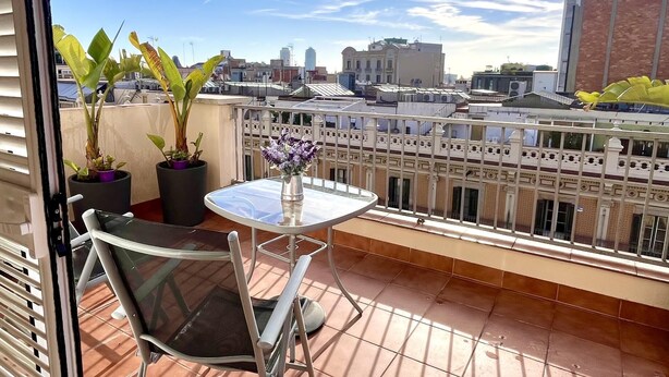 A balcony with a glass table and chairs, potted plants, and a view of the cityscape.