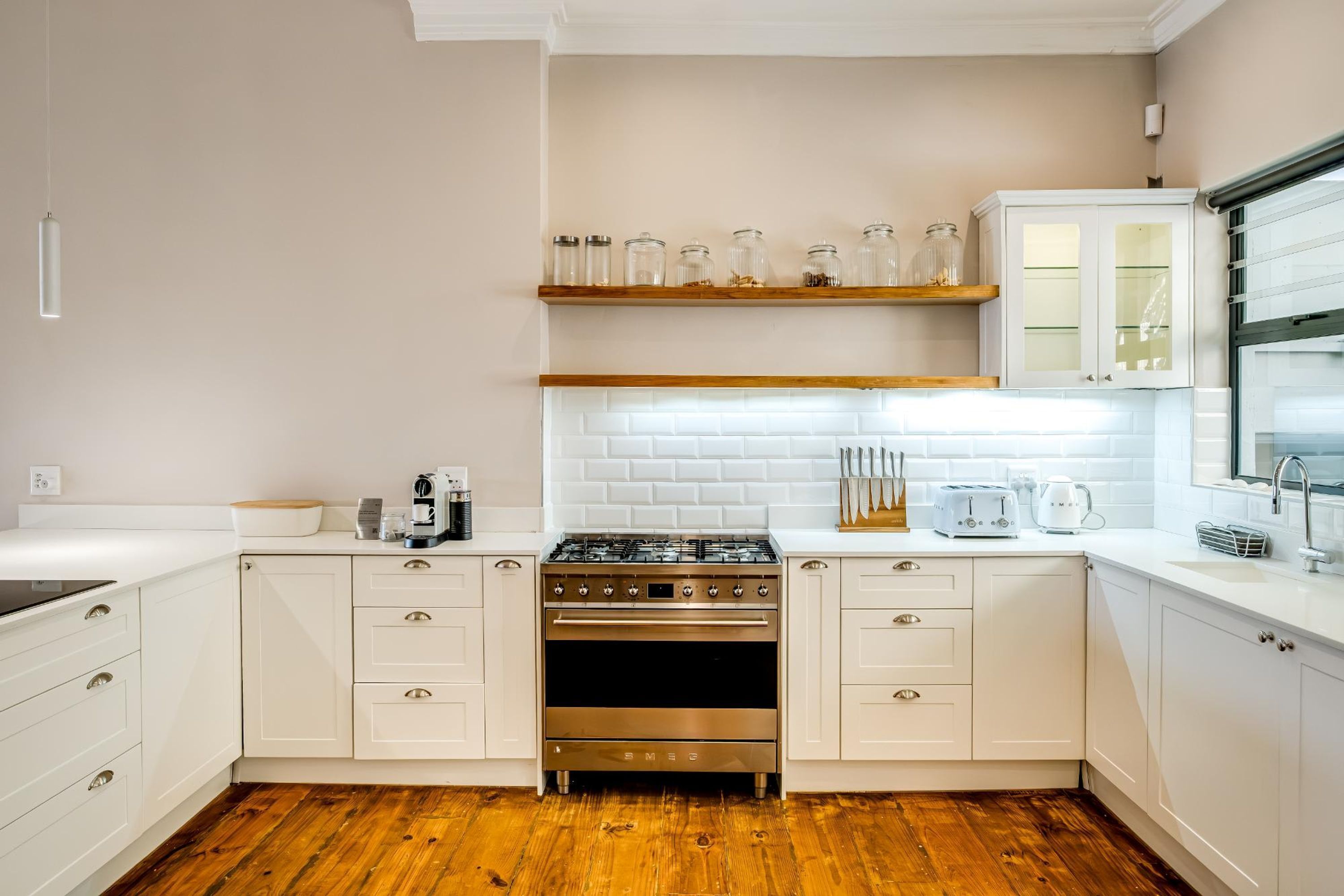 Una cocina moderna con armarios blancos, estufa de acero inoxidable y piso de madera.