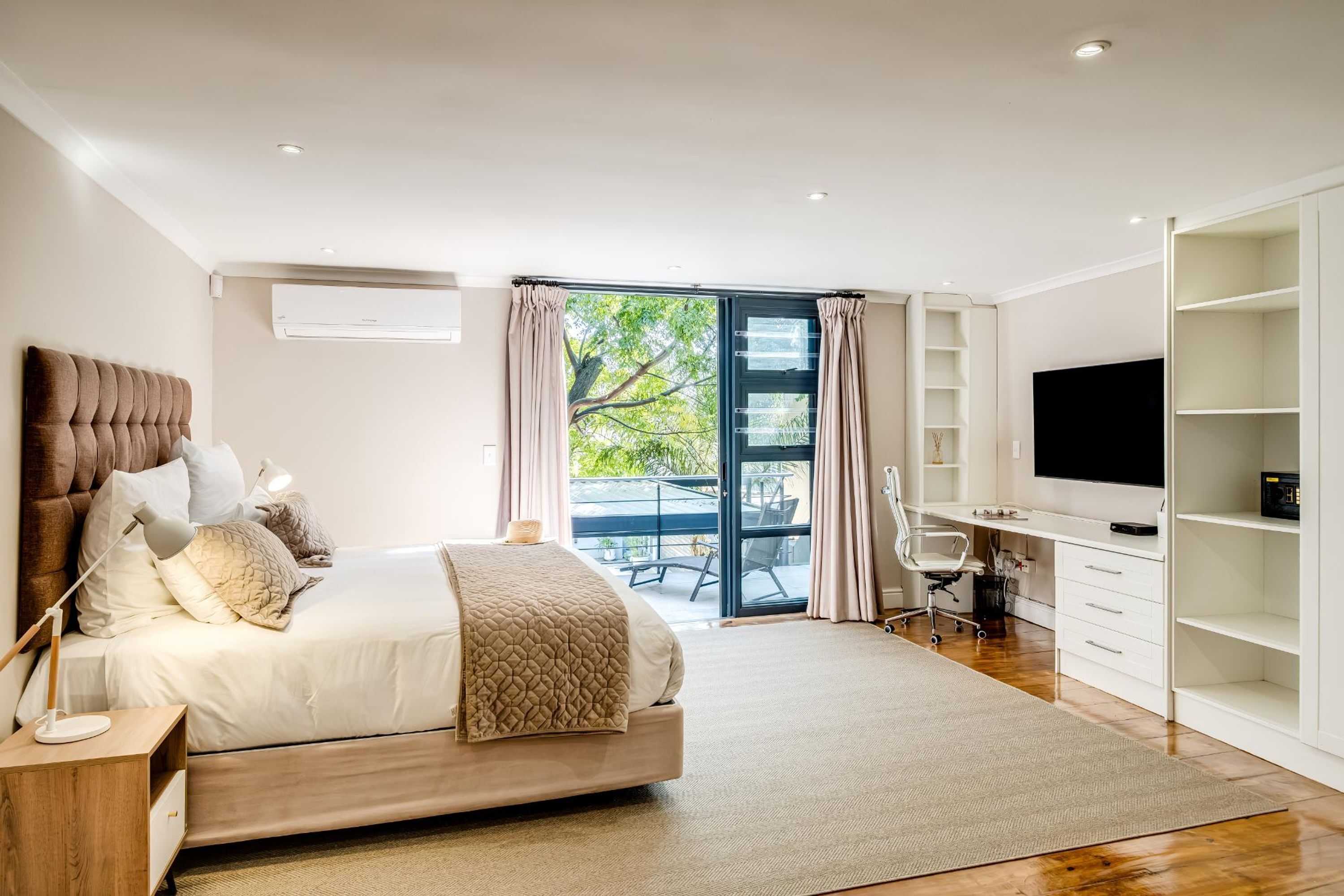 A modern bedroom with a bed, desk, TV, and a balcony.
