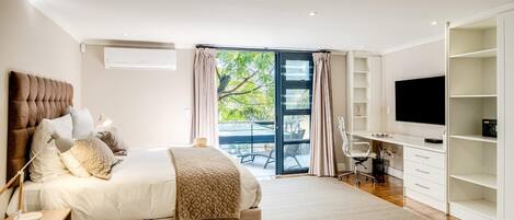 A modern bedroom with a bed, desk, TV, and a balcony.