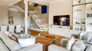 A modern living room with a staircase, a flat-screen TV, and a bookshelf. - 2bed Apt 5min Walk From Camps Bay Central Escape (Cape Town)