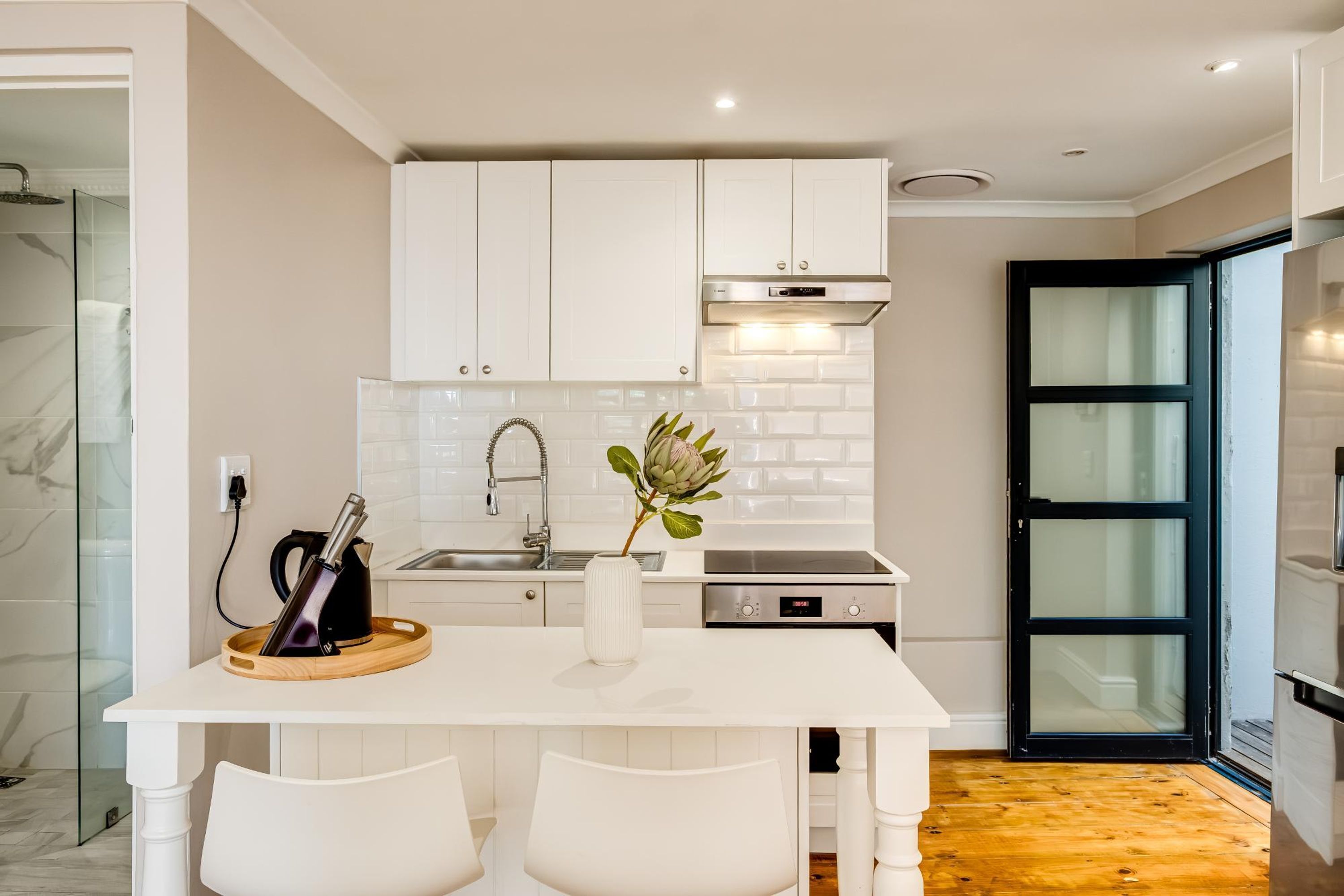 A modern kitchen with white cabinets, a stainless steel sink, and a wooden dining table with two chairs.