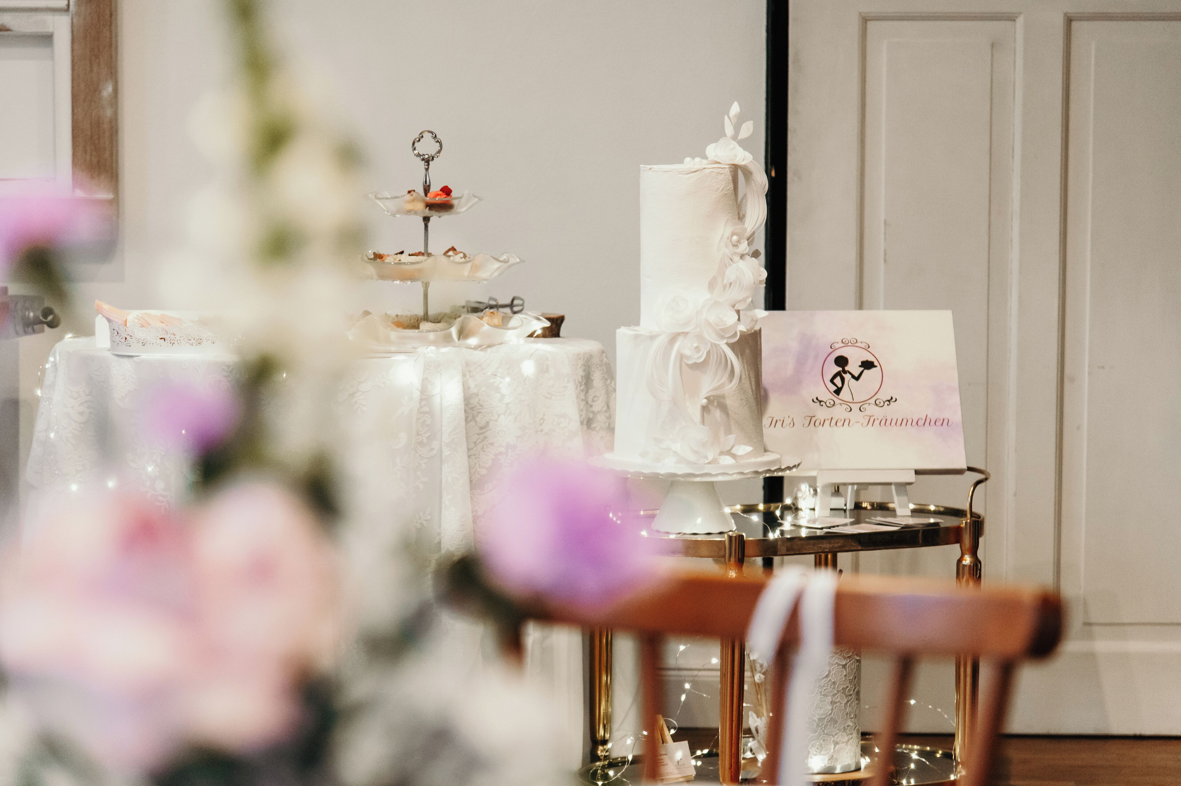 A wedding reception table with a tiered cake, a sign with a wedding theme, and a chair.