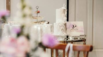A wedding reception table with a tiered cake, a sign with a wedding theme, and a chair.